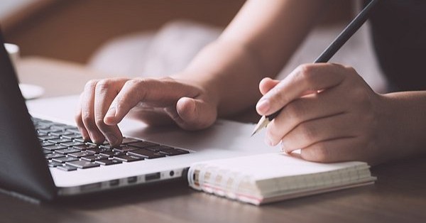 pen and paper next to a laptop