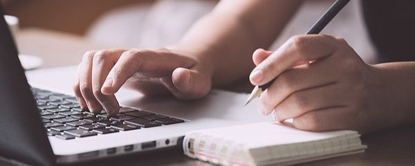 pen and paper next to a laptop